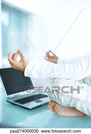 Stock Image - Man sitting in lotus position on table with laptop . Fotosearch