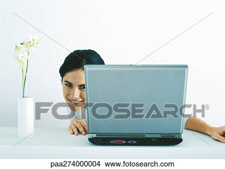 Woman peeking around side of laptop View Large Photo Image Picture - Woman peeking around side of laptop. Fotosearch
