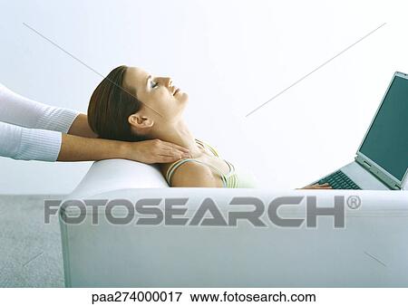 Woman sitting on sofa with laptop, having neck massaged View Large Photo Image Stock Photo - Woman sitting on sofa with laptop, having neck massaged. Fotosearch