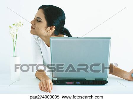 Woman sitting with laptop smelling flowers in vase View Large Photo Image Stock Photography - Woman sitting with laptop smelling flowers in vase. Fotosearch