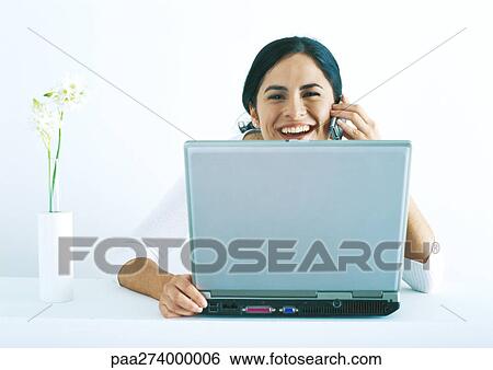 Stock Photograph - Woman sitting with laptop, talking on phone and laughing. Fotosearch