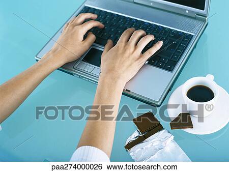 Woman typing on laptop, chocolate and coffee on desk View Large Photo Image Stock Photograph - Woman typing on laptop, chocolate and coffee on desk. Fotosearch