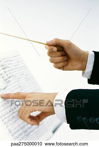 Stock Image - Conductor's hands holding baton and pointing to sheet music. Fotosearch