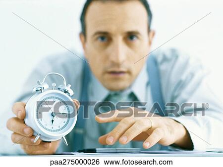 Man holding out alarm clock, focus on hands and clock in foreground View Large Photo Image Stock Photograph - Man holding out alarm clock, focus on hands and clock in foreground. Fotosearch
