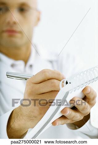 Stock Image - Man in white jacket taking notes, focus on hands in foreground. Fotosearch