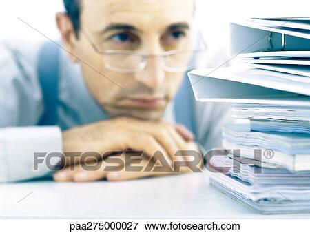 Man resting head on hands, looking at stack of files View Large Photo Image Stock Photo - Man resting head on hands, looking at stack of files. Fotosearch