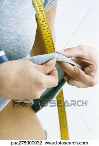 Stock Image - Woman sewing on tee-shirt she is wearing, close-up. Fotosearch