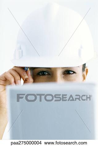 Picture - Woman wearing hard hat, looking over computer screen. Fotosearch