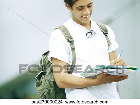 Picture - Male student standing and writing on folder. Fotosearch