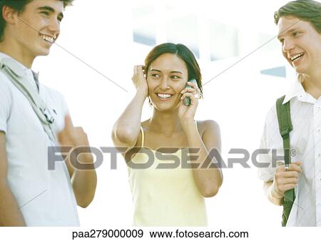 Stock Photo - Students standing together, one using cell phone. Fotosearch