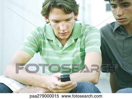 Two students sitting side by side, looking at cell phone View Large Photo Image Stock Photography - Two students sitting side by side, looking at cell phone. Fotosearch