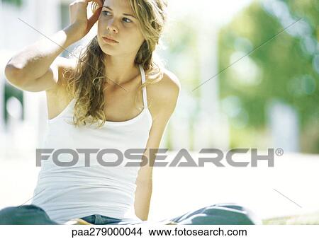 Young woman sitting outdoors, touching head View Large Photo Image Picture - Young woman sitting outdoors, touching head. Fotosearch