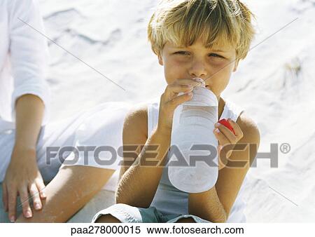 Stock Photography - Boy sitting on sand next to mother, drinking water. Fotosearch