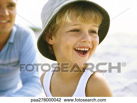 Stock Image - Boy wearing hat on beach with father. Fotosearch