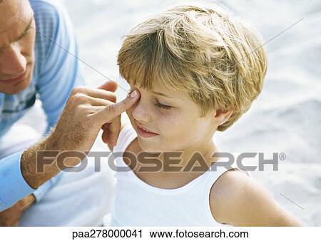 Stock Image - Father touching boy's face with one finger on beach. Fotosearch