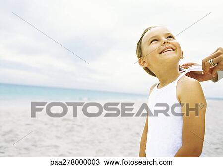 Stock Image - Girl standing on beach while mother ties shirt. Fotosearch