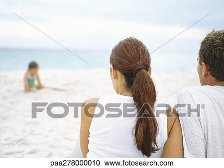 Parents sitting on beach watching little girl playing in sand View Large Photo Image Stock Image - Parents sitting on beach watching little girl playing in sand. Fotosearch