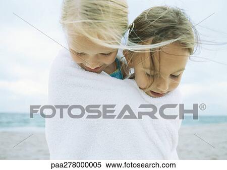 Stock Photography - Two girls wrapped in same towel on beach. Fotosearch