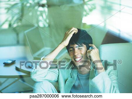 Stock Photograph - Man smiling and using cell phone, seen through glass pane. Fotosearch