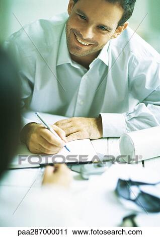 Man smiling and writing in agenda, looking at second person View Large Photo Image Stock Image - Man smiling and writing in agenda, looking at second person. Fotosearch