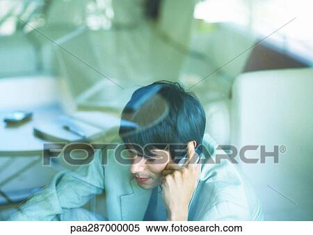 Stock Photography - Man using cell phone, seen through glass pane. Fotosearch
