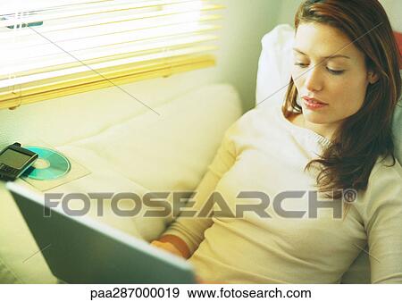 Woman sitting on couch using laptop View Large Photo Image Stock Photo - Woman sitting on couch using laptop. Fotosearch