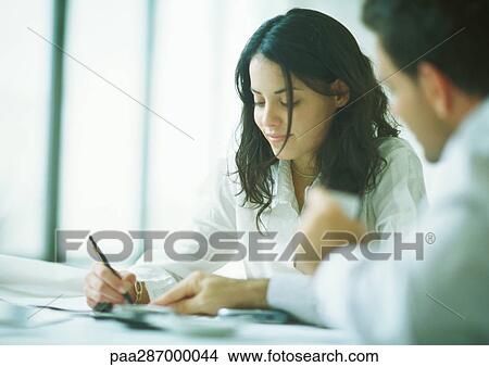 Young adults examining documents, woman holding pencil as man points View Large Photo Image Picture - Young adults examining documents, woman holding pencil as man points. Fotosearch