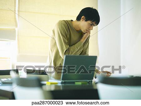 Young man using phone and laptop View Large Photo Image Stock Image - Young man using phone and laptop. Fotosearch