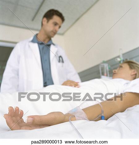 Stock Image - Doctor and female patient lying in hospital bed. Fotosearch
