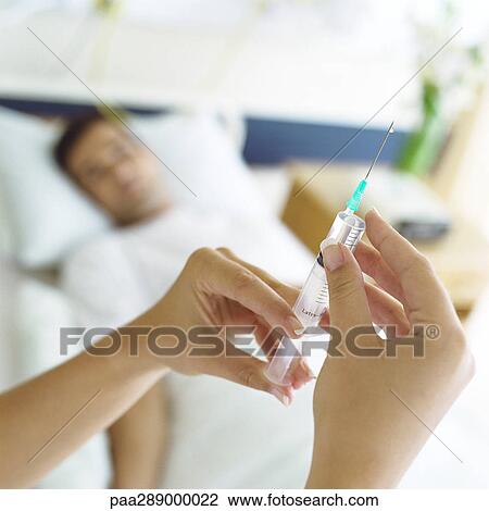 Stock Image - Syringe being held up in front of patient. Fotosearch