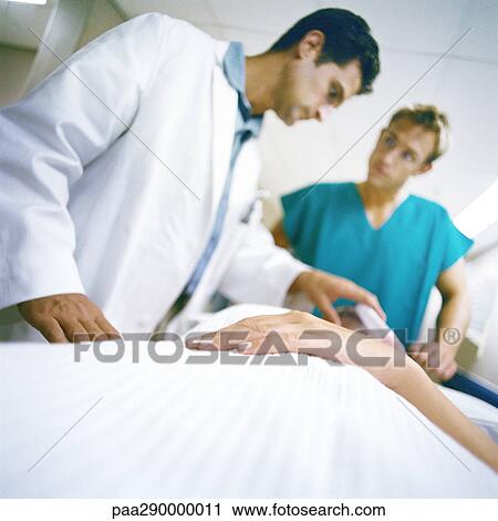 Stock Image - Doctors standing over patient. Fotosearch