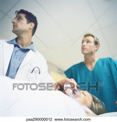 Stock Image - Doctors standing over patient. Fotosearch