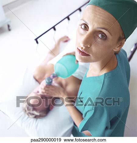 Stock Photo - Female doctor holding oxygen mask over patient's face, high angle view. Fotosearch