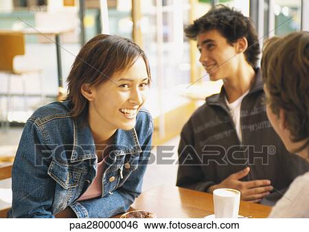 Stock Photograph - Group of young people sitting at table in cafÄ, smiling. Fotosearch