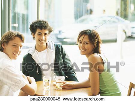 Group of young people sitting at table in cafÄ, smiling at camera View Large Photo Image Stock Photography - Group of young people sitting at table in cafÄ, smiling at camera. Fotosearch
