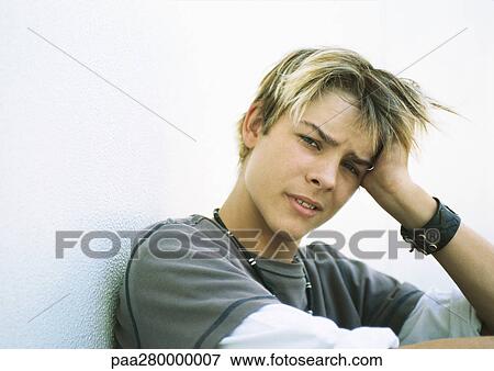Stock Photo - Teenage boy holding head, looking at camera. Fotosearch