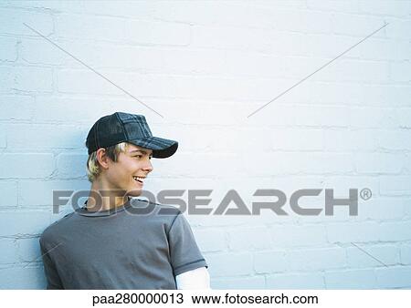 Stock Image - Teenage boy leaning against brick wall, side view, portrait. Fotosearch