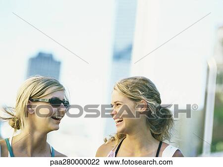 Stock Image - Teenage girls smiling at each other, in city setting. Fotosearch