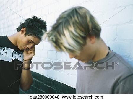 Two teenage boys standing next to brick wall, one using cell phone View Large Photo Image Stock Photo - Two teenage boys standing next to brick wall, one using cell phone. Fotosearch