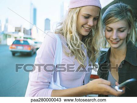 Two teenage girls standing near street looking at cell phone View Large Photo Image Stock Image - Two teenage girls standing near street looking at cell phone. Fotosearch