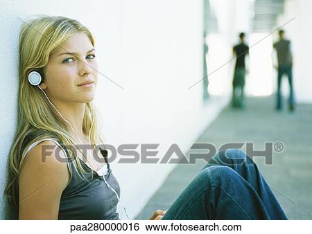 Young woman listening to headphones, looking at camera View Large Photo Image Stock Photograph - Young woman listening to headphones, looking at camera. Fotosearch
