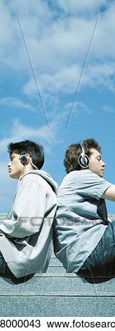 Two young men wearing headphones, sitting back to back View Large Photo Image Stock Image - Two young men wearing headphones, sitting back to back. Fotosearch