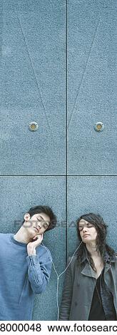 Young couple leaning against wall, sharing earphones with eyes closed View Large Photo Image Stock Photo - Young couple leaning against wall, sharing earphones with eyes closed. Fotosearch