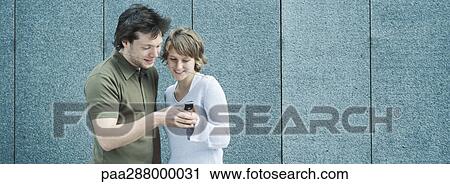 Young couple looking at camera phone View Large Photo Image Stock Image - Young couple looking at camera phone. Fotosearch