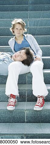 Stock Image - Young couple on steps, man resting head on woman's lap. Fotosearch