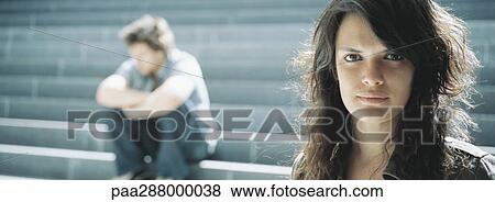 Young woman looking at camera, young man sitting in background View Large Photo Image Stock Photo - Young woman looking at camera, young man sitting in background. Fotosearch