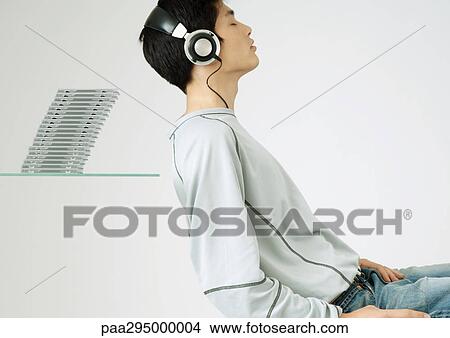 Young man listening to headphones, sitting in front of stack of cds View Large Photo Image Picture - Young man listening to headphones, sitting in front of stack of cds. Fotosearch
