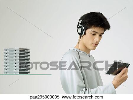Young man listening to headphones, looking at cd View Large Photo Image Stock Photography - Young man listening to headphones, looking at cd. Fotosearch