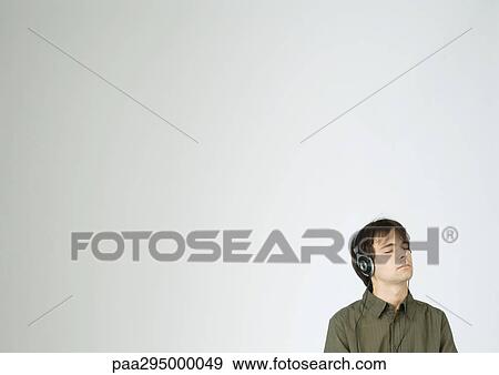 Young man listening to headphones with eyes closed, portrait View Large Photo Image Stock Photo - Young man listening to headphones with eyes closed, portrait. Fotosearch