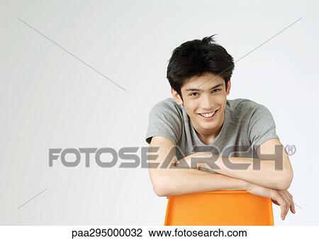 Young man sitting backwards on chair, smiling, portrait View Large Photo Image Stock Image - Young man sitting backwards on chair, smiling, portrait. Fotosearch